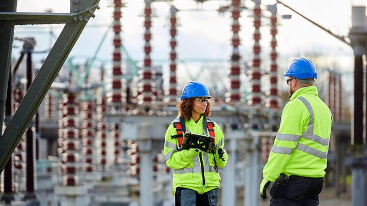 Two workers in a protective gear talking in a electrical power substation
