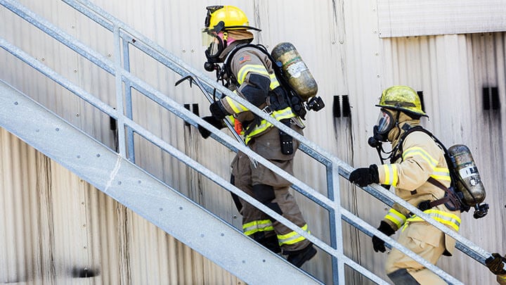 Two firemen in protective gear going up a metal staircase