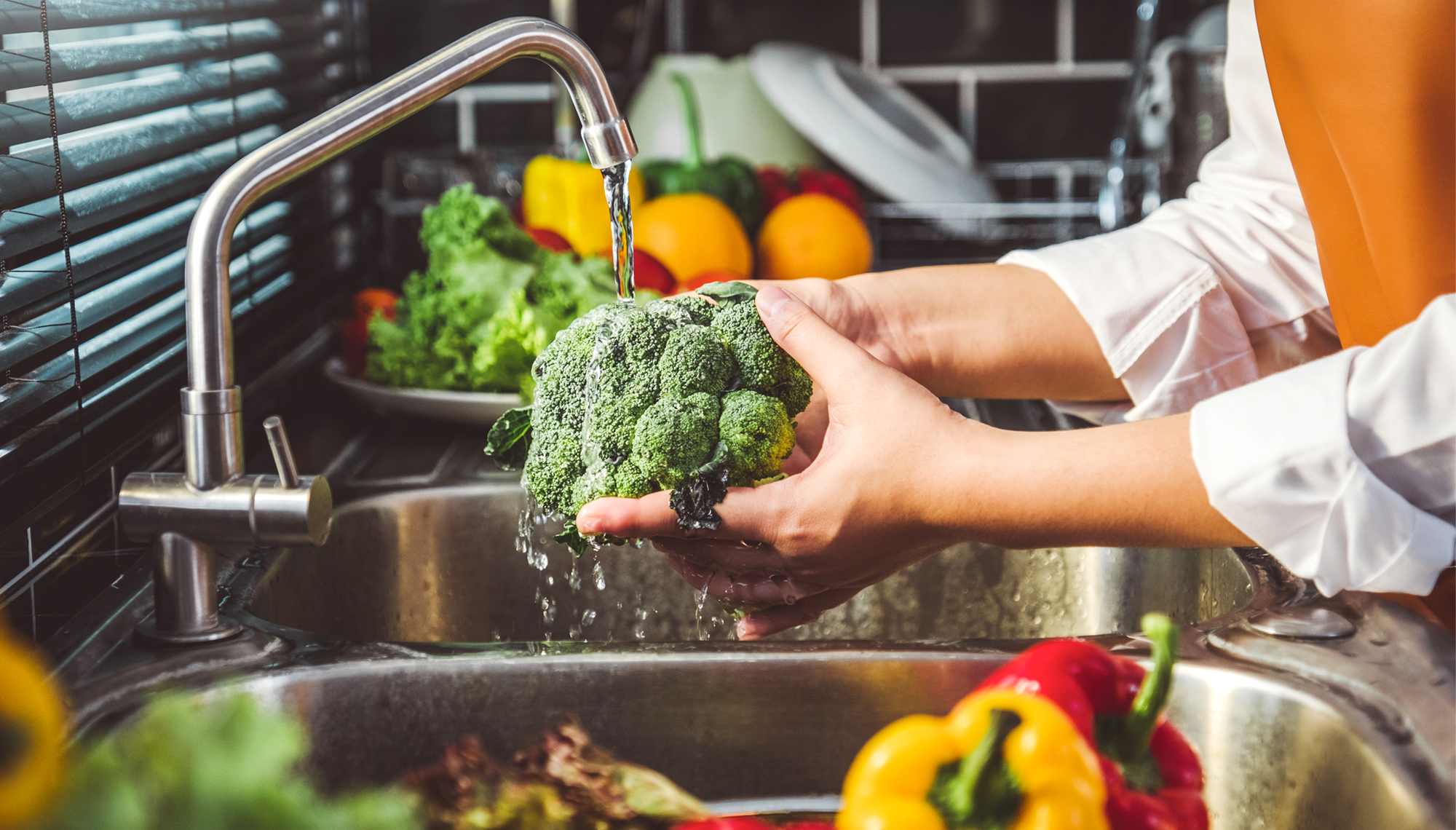 Person washing fresh vegetables and fruits in kitchen sink