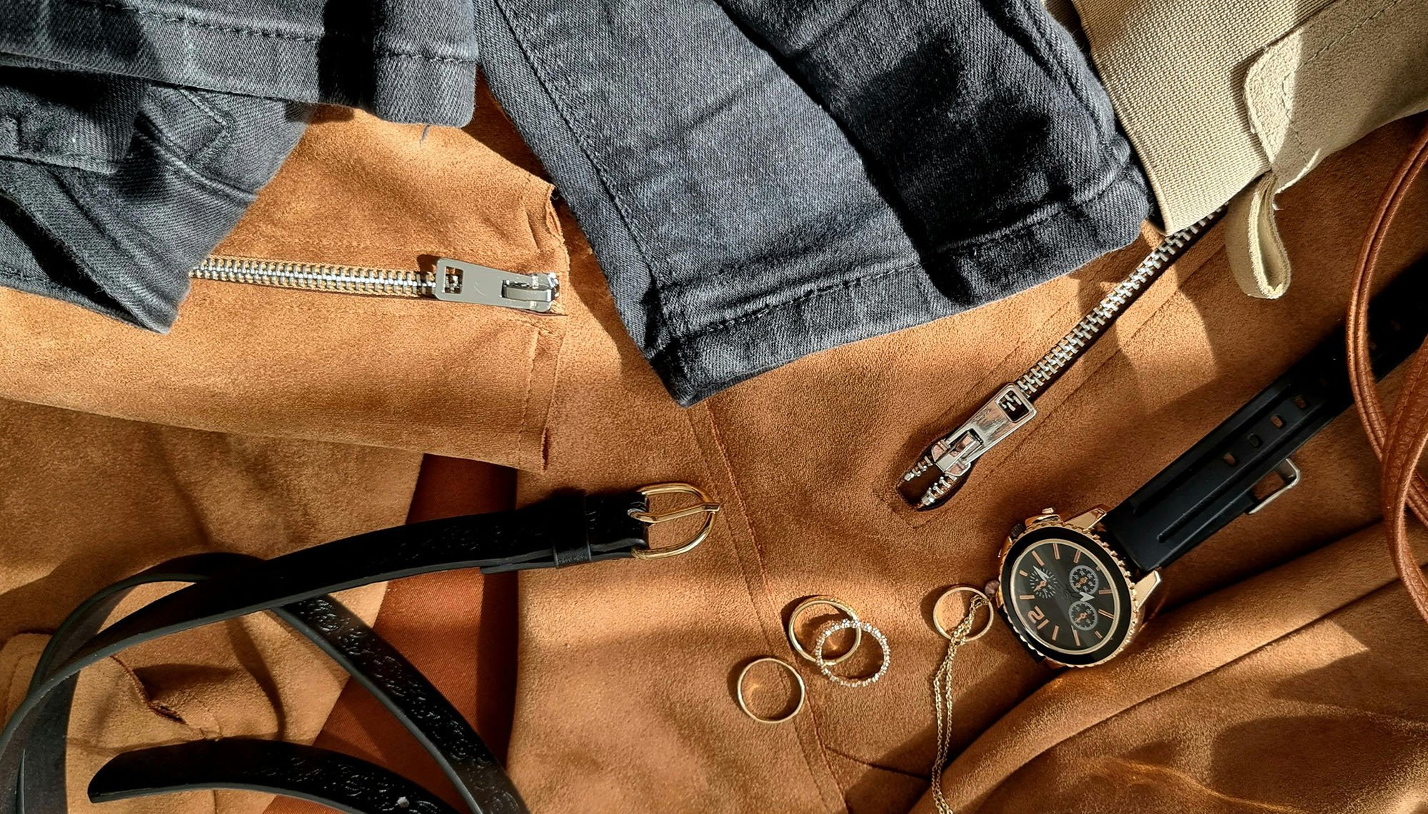 an image showing varous casual clothing items and accessories such as watch, rings, zippers, belt, with sunlight shining on them