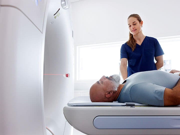 Medical professional assisting mature man with grey beard on the table of a CT scanner