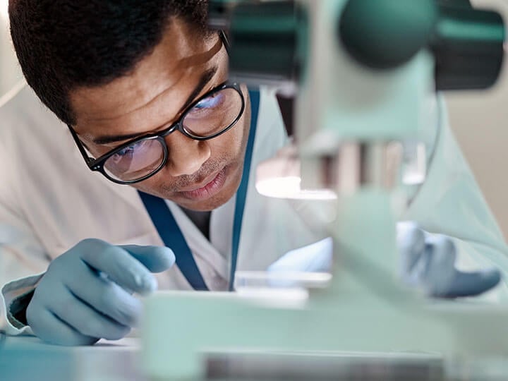 Intertek-PSI’s Industrial Hygiene Laboratory with a man in black glasses in a lab coat looking at a microscope