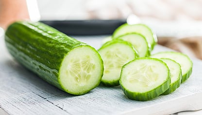 Image of someone cutting a cucumber on a chopping board.