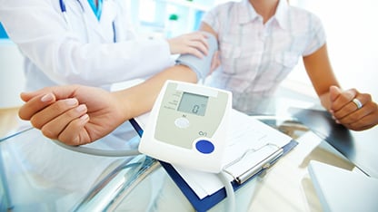 A healthcare professional checks a patient's blood pressure with a cuff and monitor in a medical office.