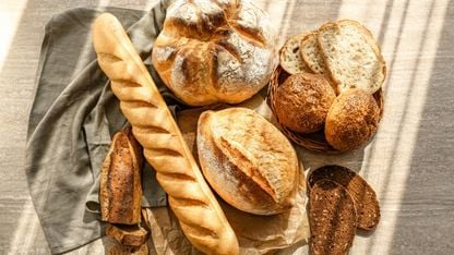 Close-up of a variety of bread, including a baguette, round sourdough, and seeded rolls, arranged on a linen cloth.